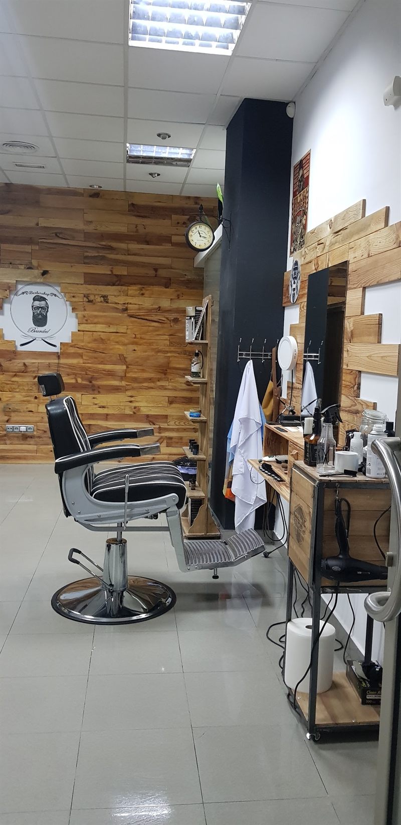Sillón de barbero junto a la pared de palé con el logotipo de The Bearded